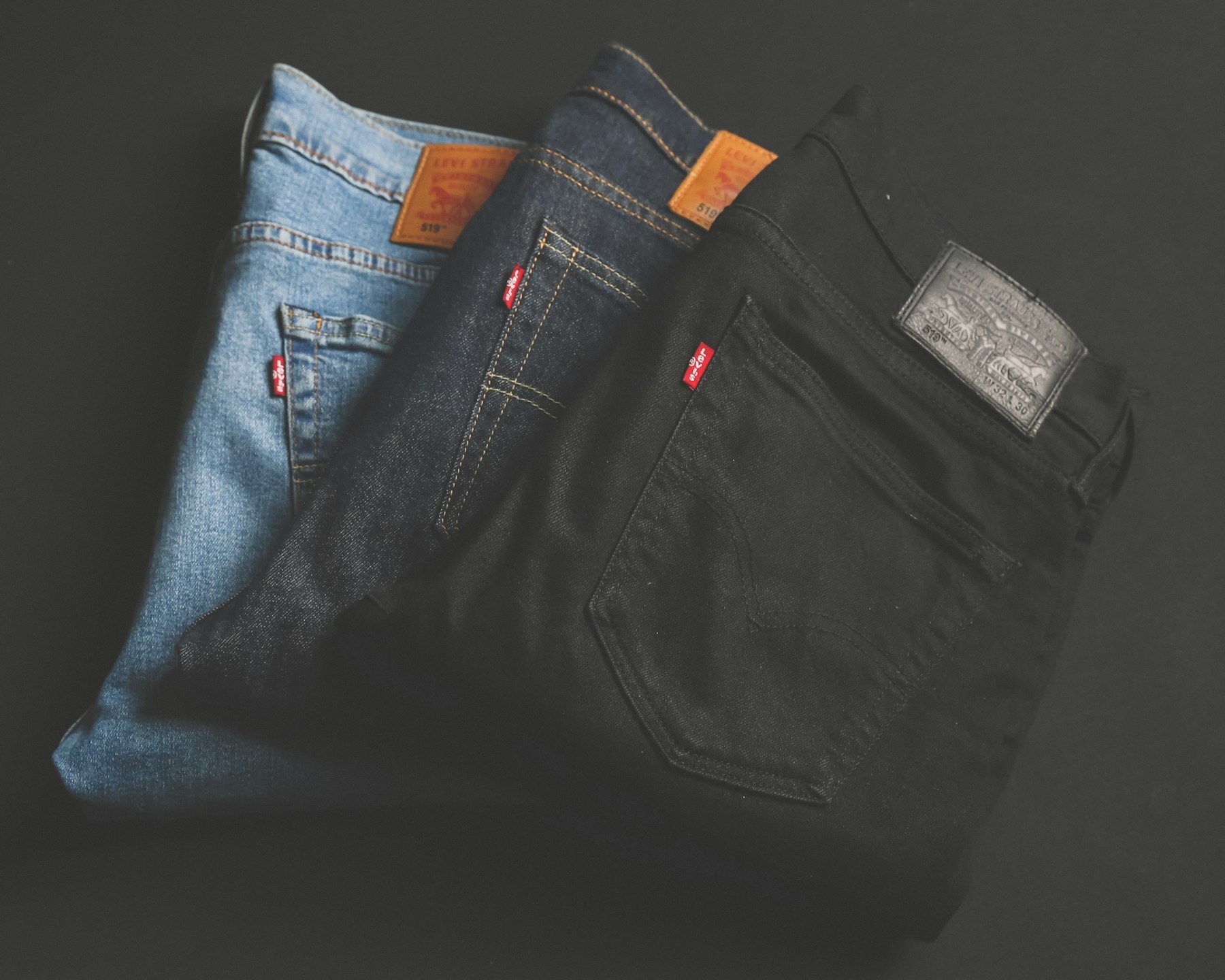 Tres jeans Levi's doblados sobre un fondo oscuro, claro, azul y negro, con sus etiquetas de cuero